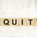 “Wooden blocks spelling the word ‘EQUITY’ on a light wooden surface with a neutral background.”